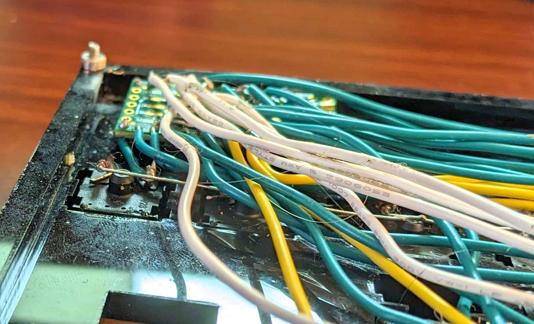 A photograph showing a mess of wires on the underside of a keyboard. The wires have picked up quite a lot of hair and lint and are messily attached to the terminals of a small control board, barely visible through them.